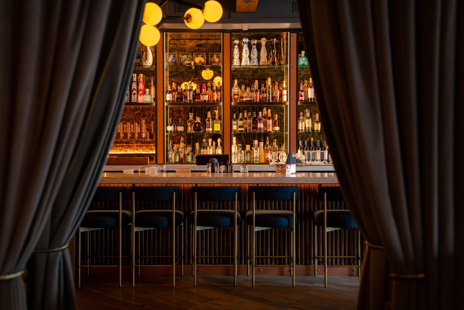The bar at Ce Soir Brasserie + Bar framed by velvet curtains